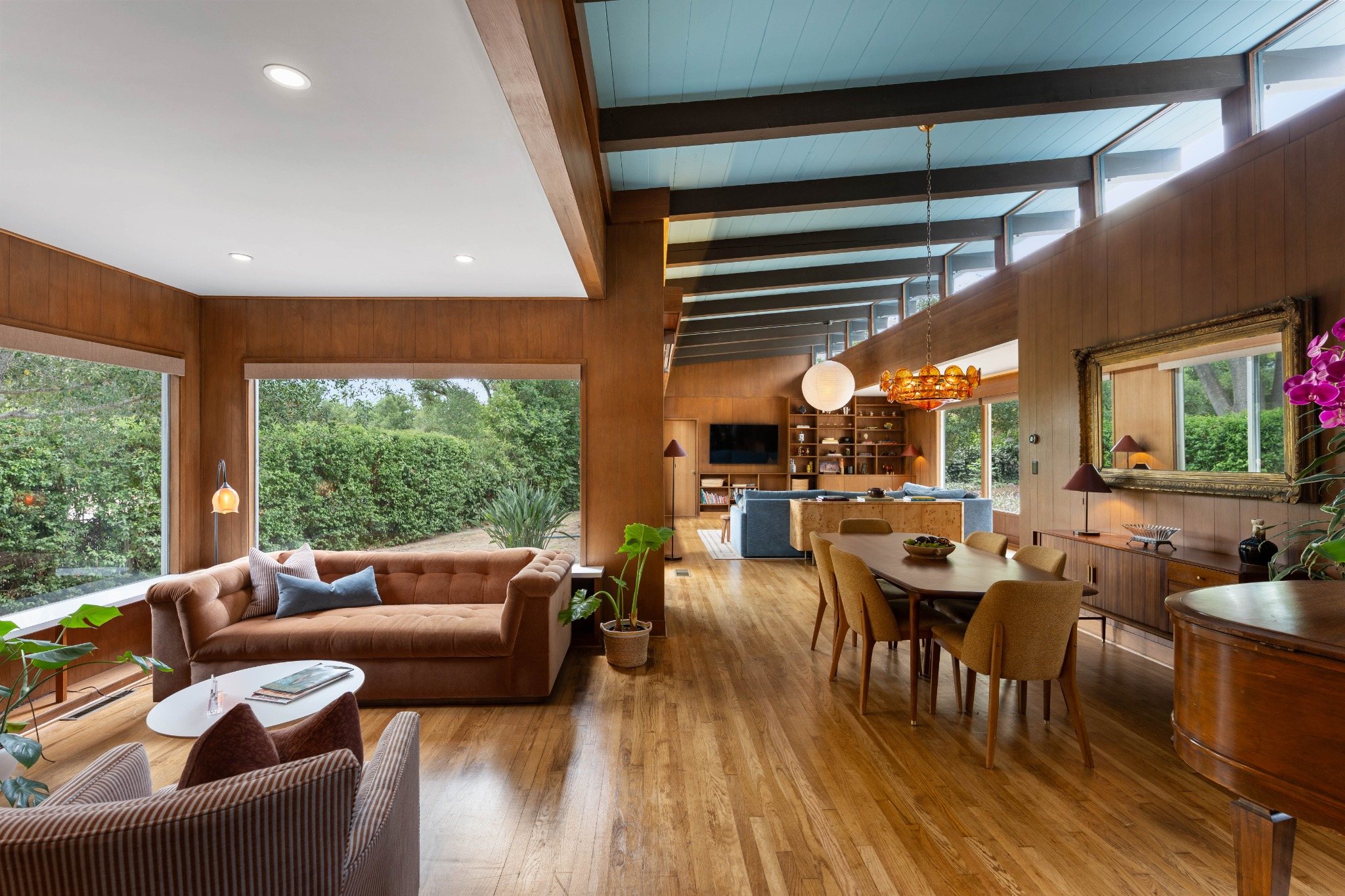 Living and dining room with vaulted ceiling, wood paneling, and Mid-Century Modern design